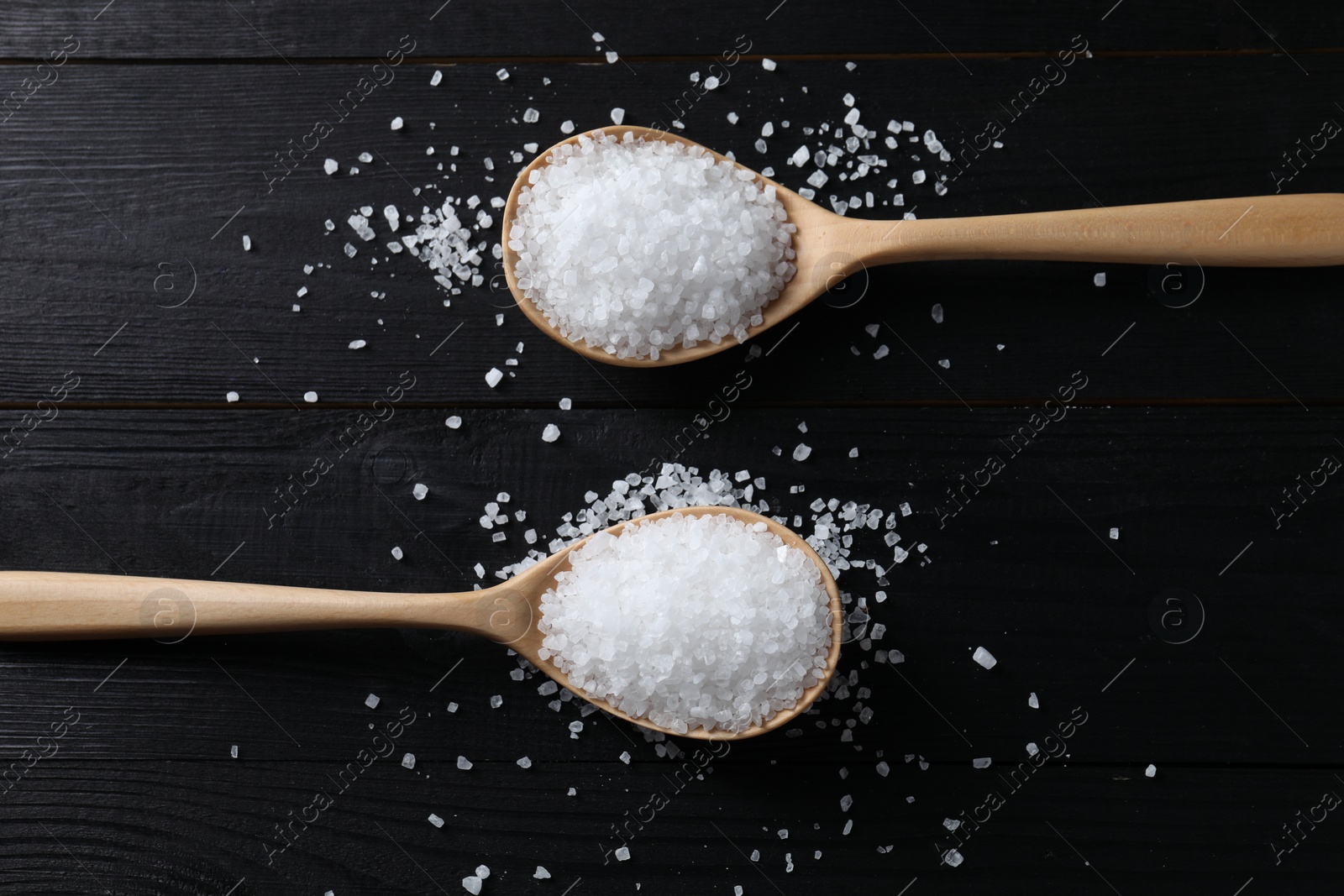 Photo of Organic salt in spoons on black wooden table, top view