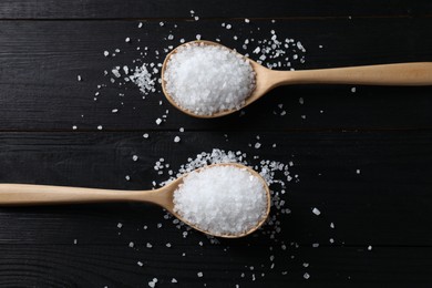 Photo of Organic salt in spoons on black wooden table, top view