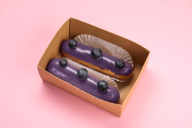 Photo of Delicious eclairs decorated with blueberries on pink background