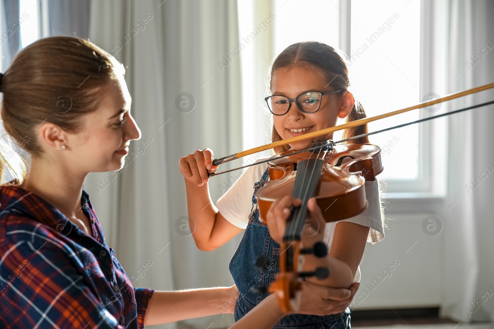 Photo of Young woman teaching little girl to play violin indoors