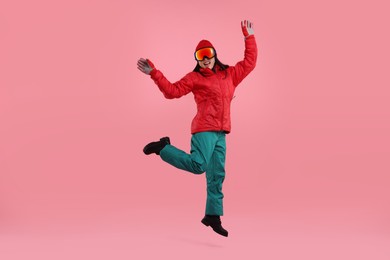 Photo of Happy woman in winter sportswear and goggles jumping on pink background