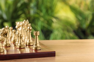 Photo of Chess board with golden pieces on wooden table against blurred background, space for text