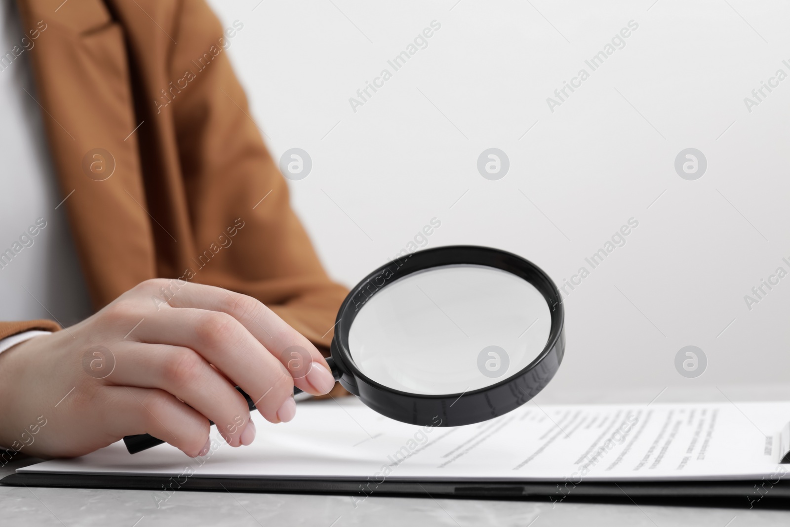 Photo of Woman looking at document through magnifier at light gray table, closeup. Searching concept