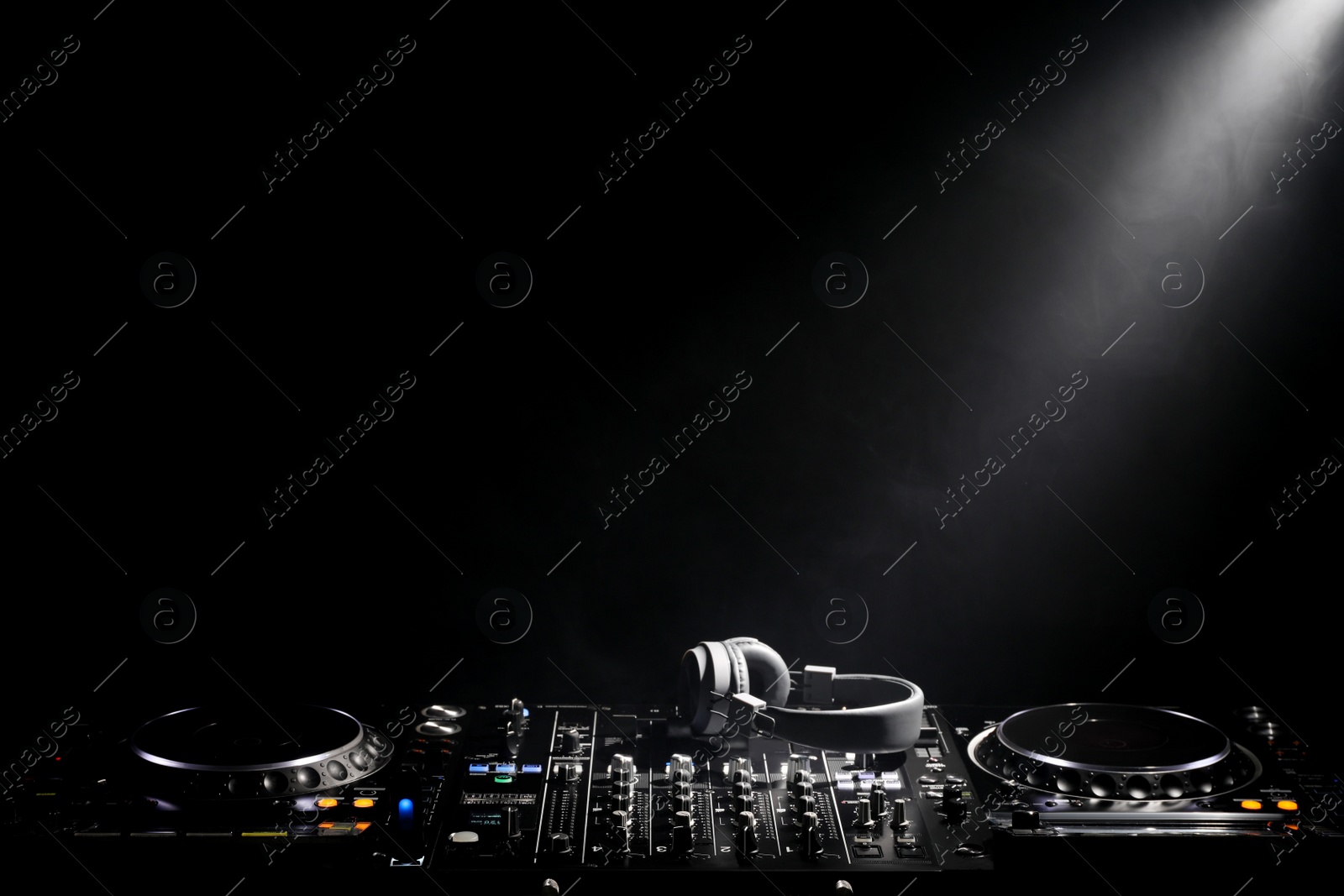 Photo of Modern DJ controller and headphones under beam of light on black background