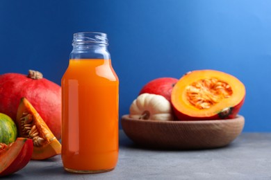 Photo of Tasty pumpkin juice in glass bottle and different pumpkins on light grey table against blue background. Space for text