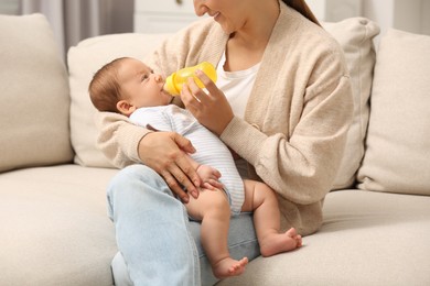Mother feeding her cute child with infant formula indoors
