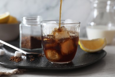 Photo of Pouring coffee into glass with ice cubes at white wooden table, closeup