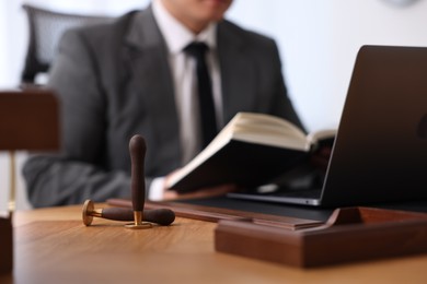 Photo of Notary working with laptop and book at wooden table in office, focus on wax stamps