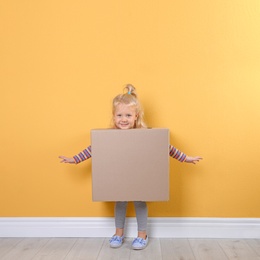 Photo of Cute little girl playing with cardboard box near color wall