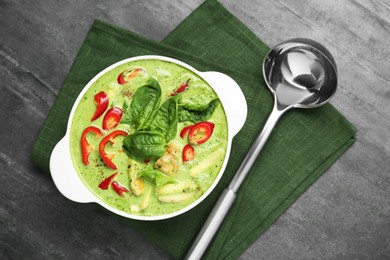 Saucepan with delicious green curry chicken soup and ladle on light grey table, flat lay