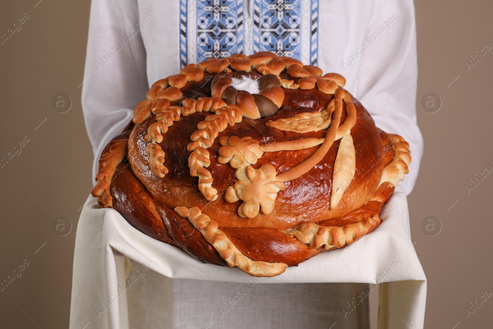 Photo of Woman with korovai on grey background, closeup. Ukrainian bread and salt welcoming tradition