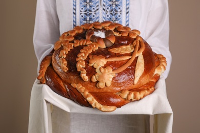 Woman with korovai on grey background, closeup. Ukrainian bread and salt welcoming tradition