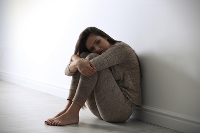 Photo of Depressed young woman sitting on floor near light wall