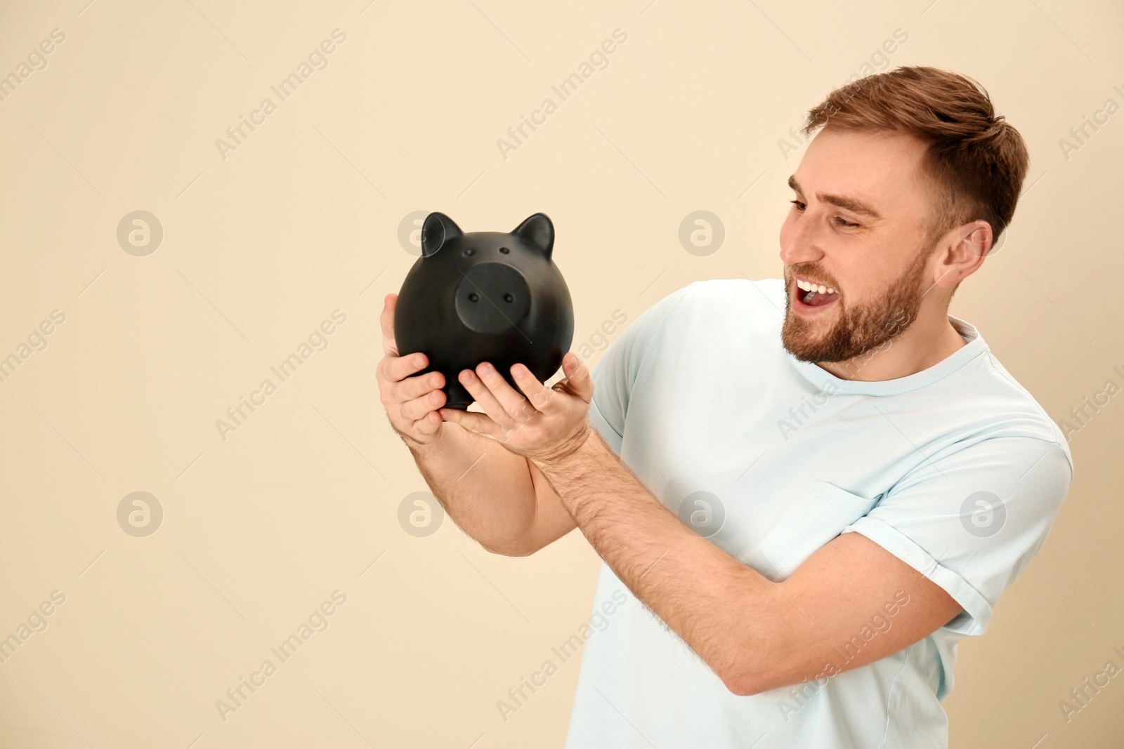 Photo of Happy young man with piggy bank and space for text on color background. Money saving