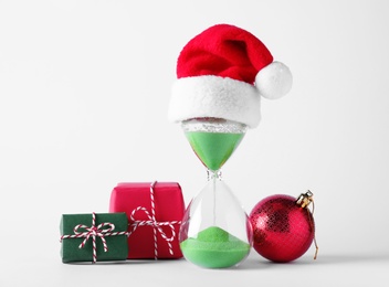Photo of Hourglass with Santa hat and festive decor on white background. Christmas countdown
