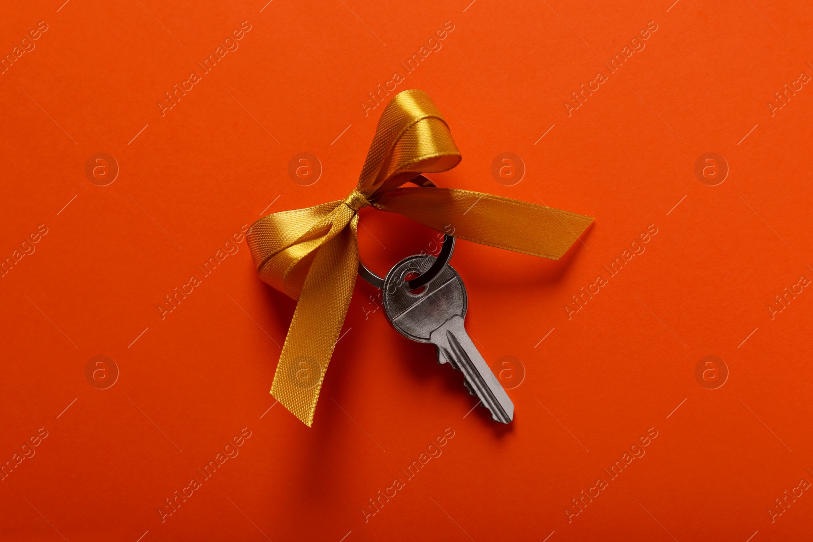 Photo of Key with yellow bow on orange background, top view. Housewarming party