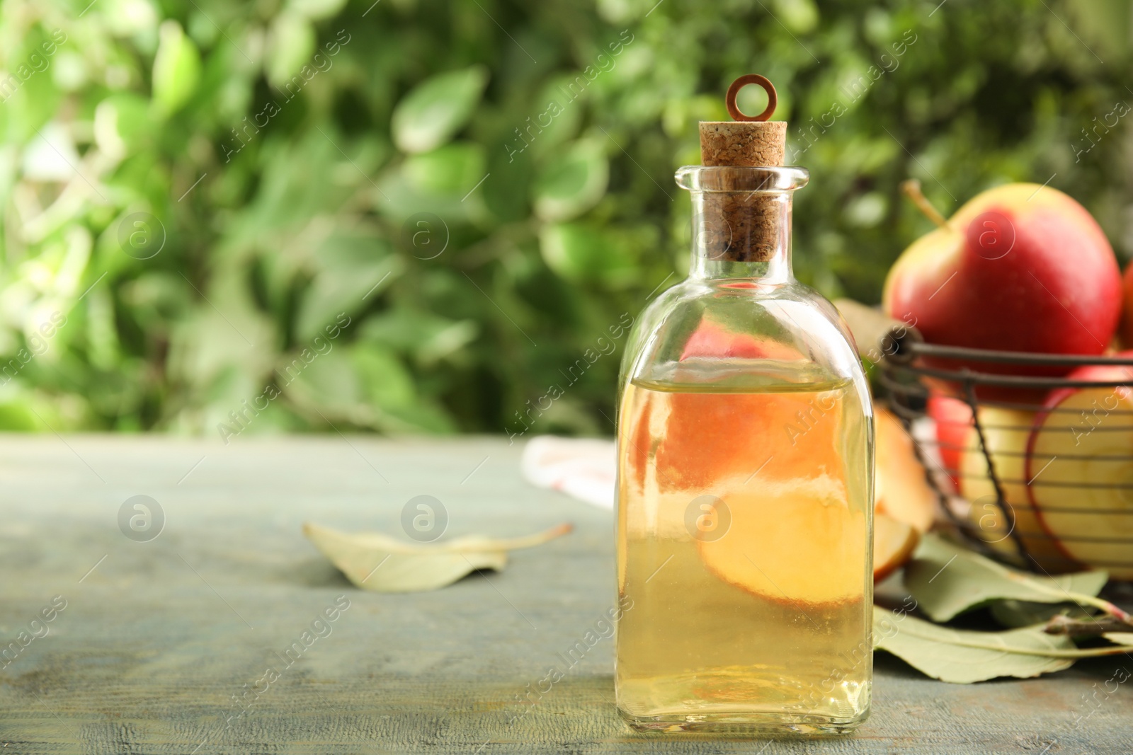 Photo of Natural apple vinegar and fresh fruits on blue wooden table. Space for text