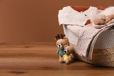 Laundry basket with baby clothes and soft toys on wooden table, space for text