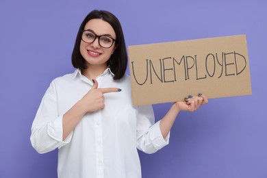 Young woman holding sign with word Unemployed on violet background