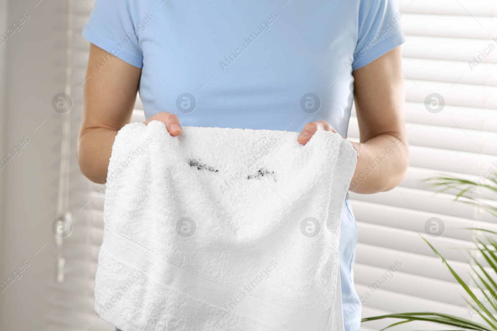 Photo of Woman holding terry towel with mascara spot indoors, closeup. Makeup removal