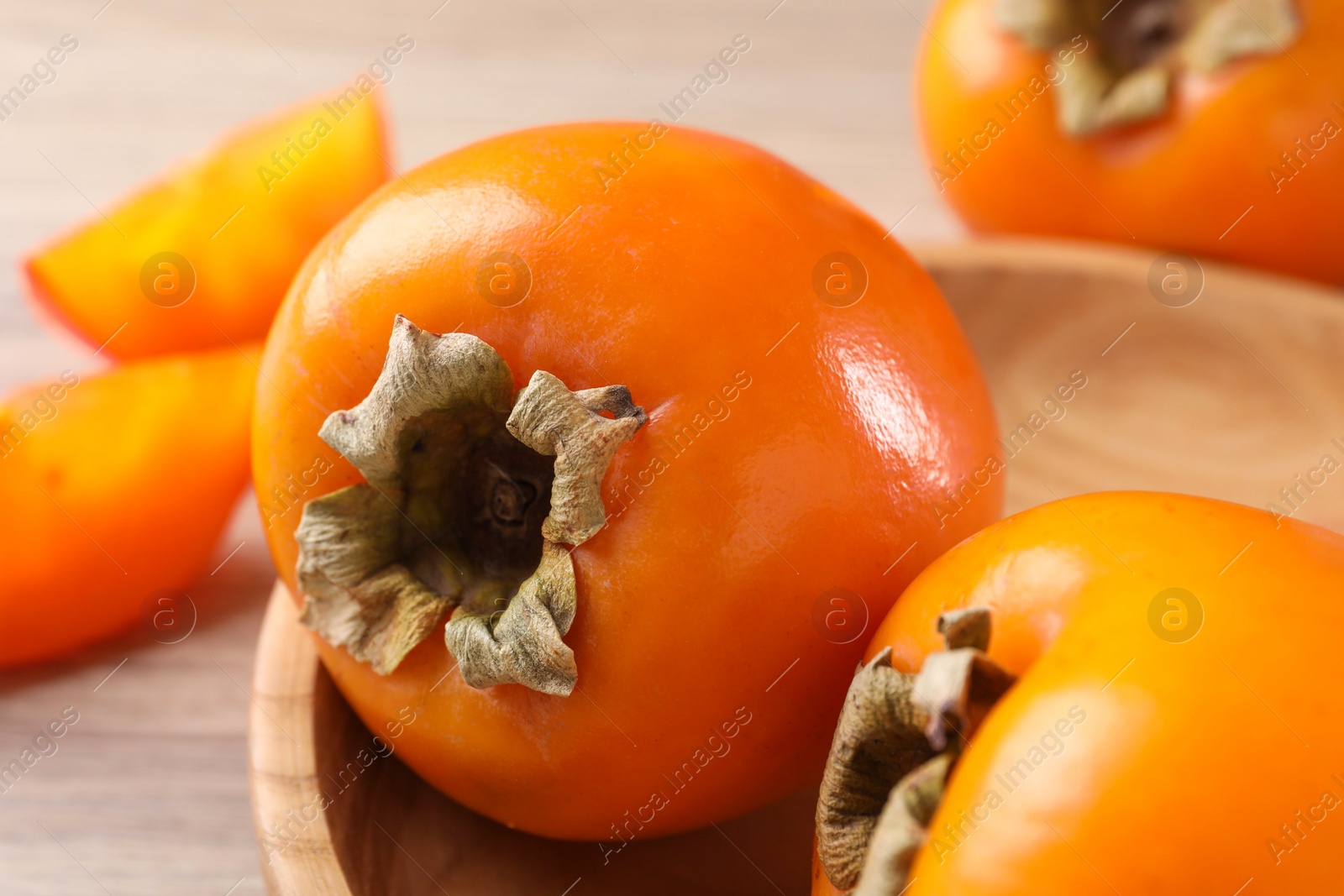 Photo of Delicious ripe persimmons in bowl on table, closeup