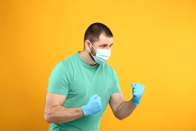 Man with protective mask and gloves in fighting pose on yellow background. Strong immunity concept