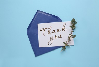 Card with phrase Thank You, envelope and branch of eucalyptus on light blue background, flat lay