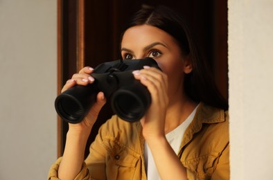 Photo of Concept of private life. Curious young woman with binoculars spying on neighbours outdoors