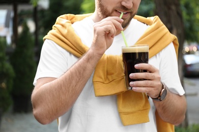 Photo of Young man with cold kvass outdoors, closeup. Traditional Russian summer drink