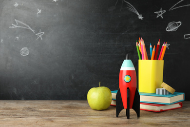 Photo of Bright toy rocket and school supplies on wooden desk. Space for text