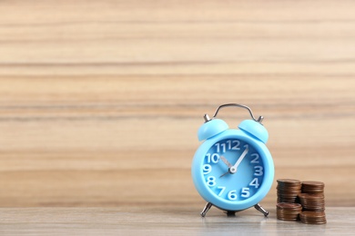 Photo of Light blue alarm clock and stacked coins on table against wooden background, space for text. Money savings