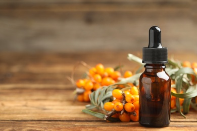 Photo of Natural sea buckthorn oil and fresh berries on wooden table. Space for text