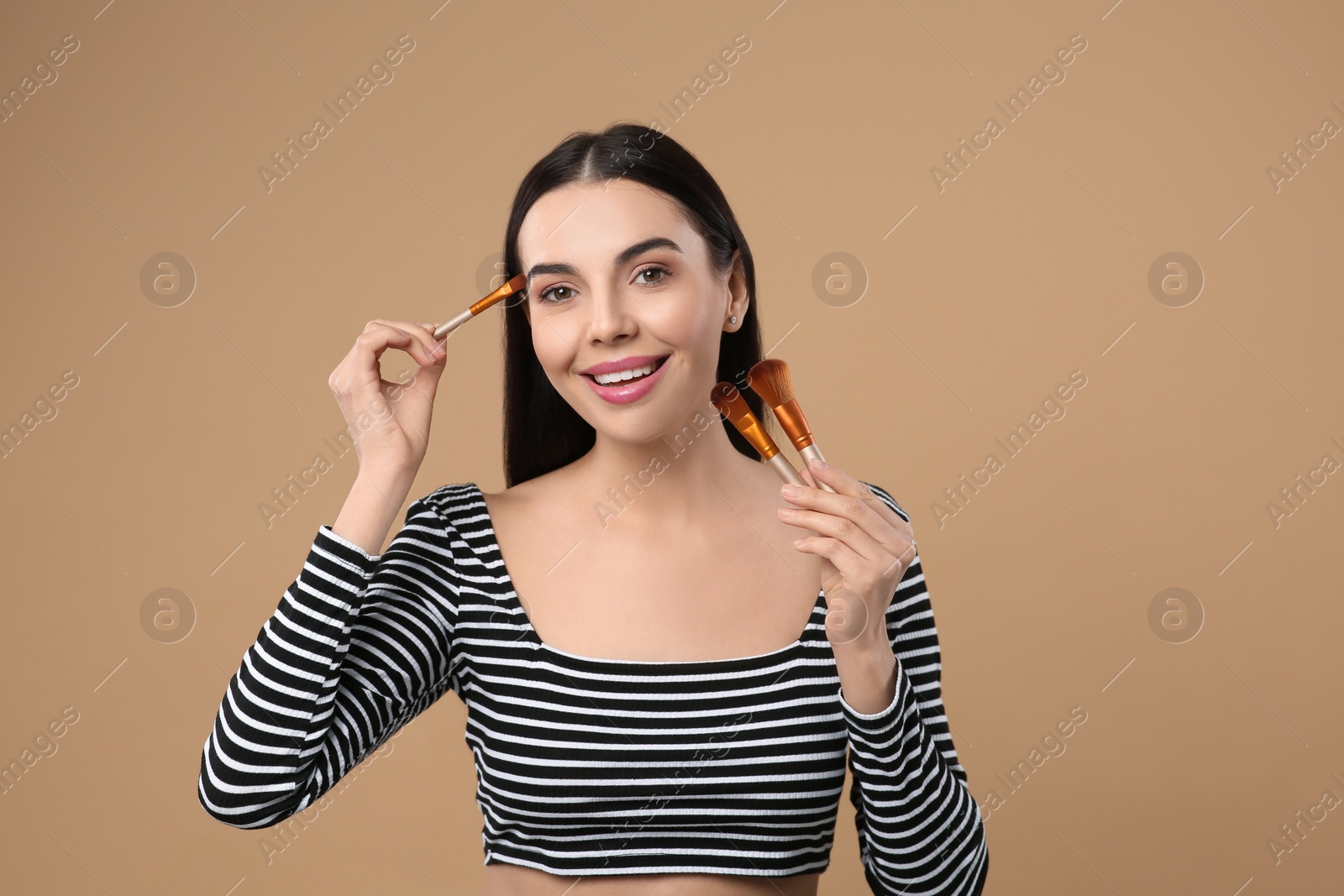 Photo of Happy woman with different makeup brushes on light brown background