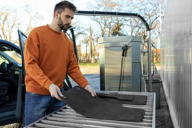 Man with auto carpets near vacuum cleaner at self-service car wash