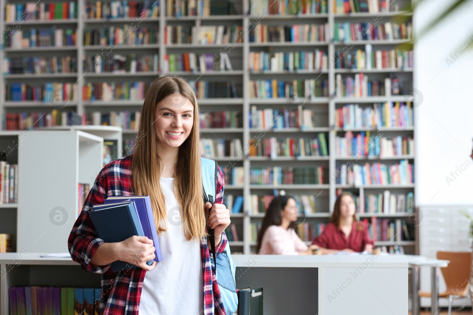 Photo of Young pretty woman with books and backpack in library. Space for text