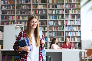 Photo of Young pretty woman with books and backpack in library. Space for text