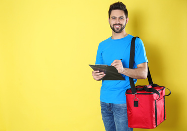 Photo of Courier with thermo bag and clipboard on yellow background, space for text. Food delivery service