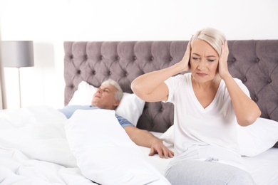 Photo of Upset mature woman sitting on bed near her sleeping husband at home. Relationship problems