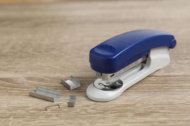 Photo of Bright stapler and metal staples on wooden table, closeup