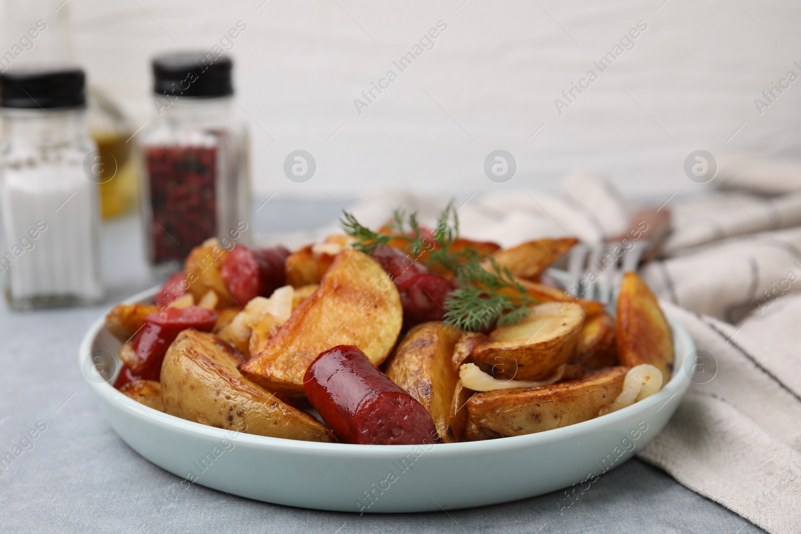 Photo of Delicious baked potato with thin dry smoked sausages, onion and dill on gray table, closeup