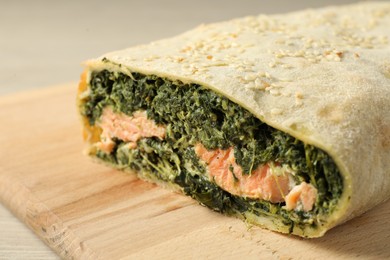 Photo of Delicious strudel with salmon and spinach served on light wooden table, closeup