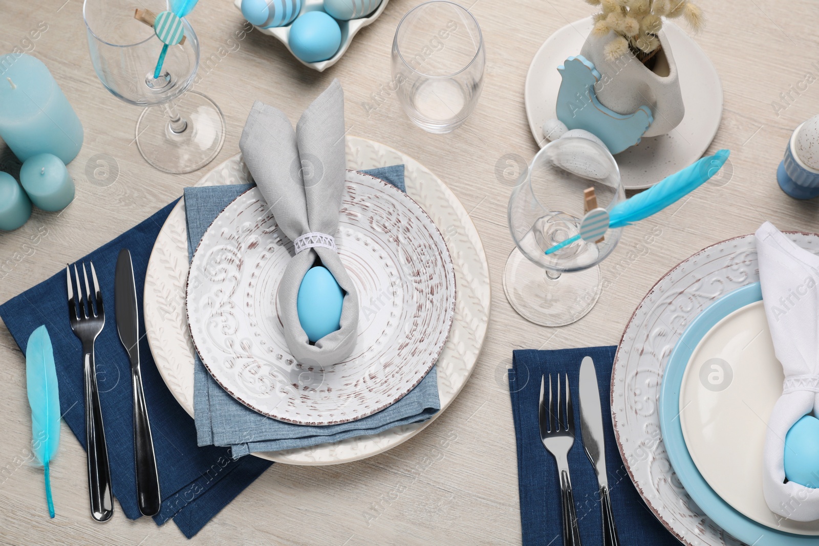 Photo of Festive table setting with bunny ears made of light blue eggs and napkins, above view. Easter celebration