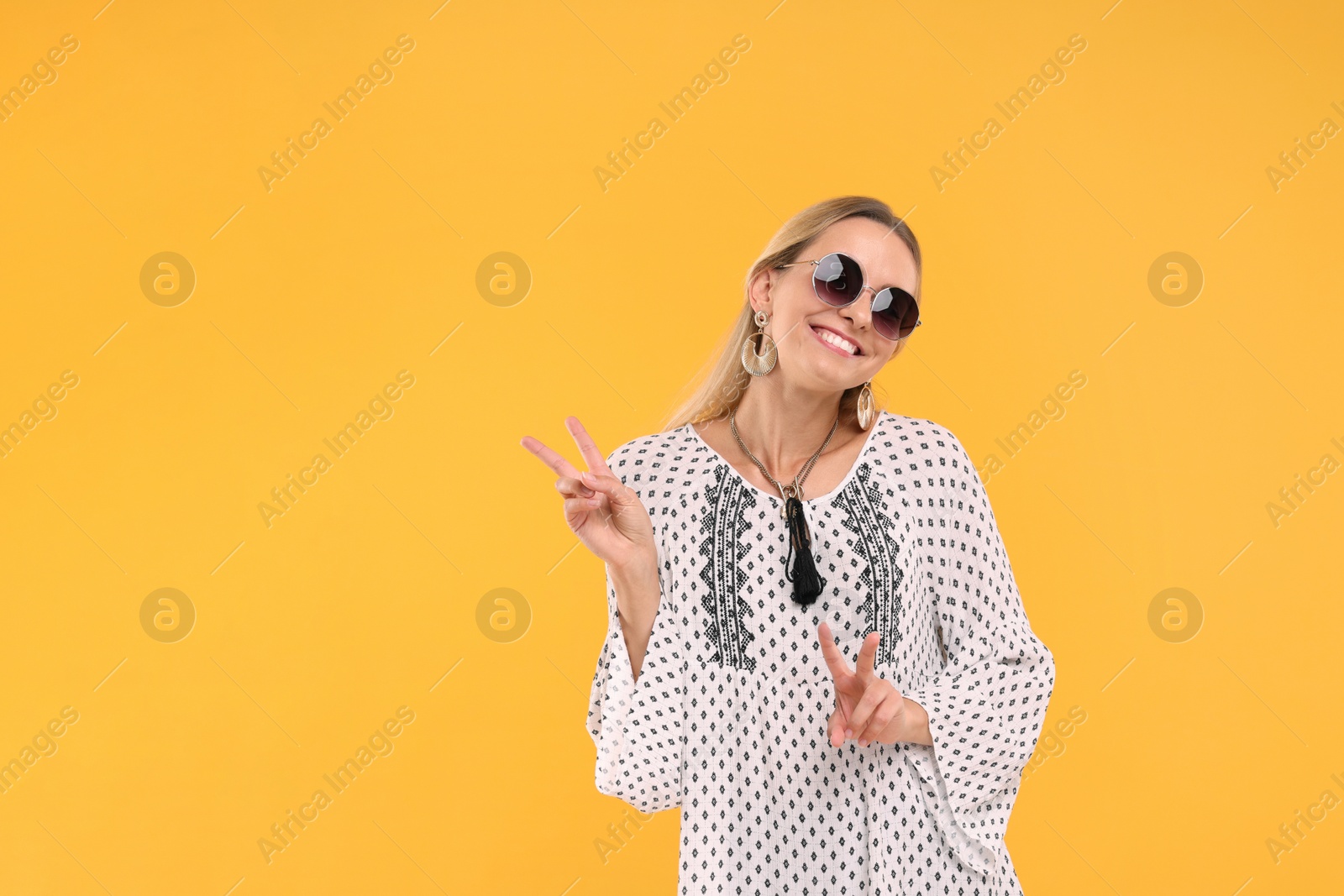 Photo of Portrait of smiling hippie woman showing peace signs on yellow background. Space for text