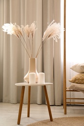 Photo of Dry plants and candles on table in room. Interior design