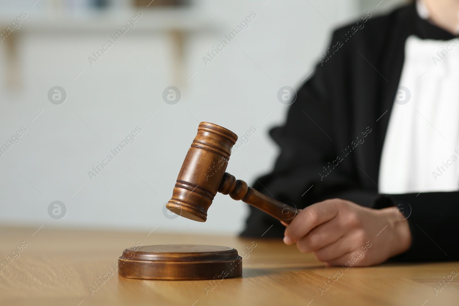 Photo of Judge striking mallet at wooden table in courtroom, closeup. Space for text