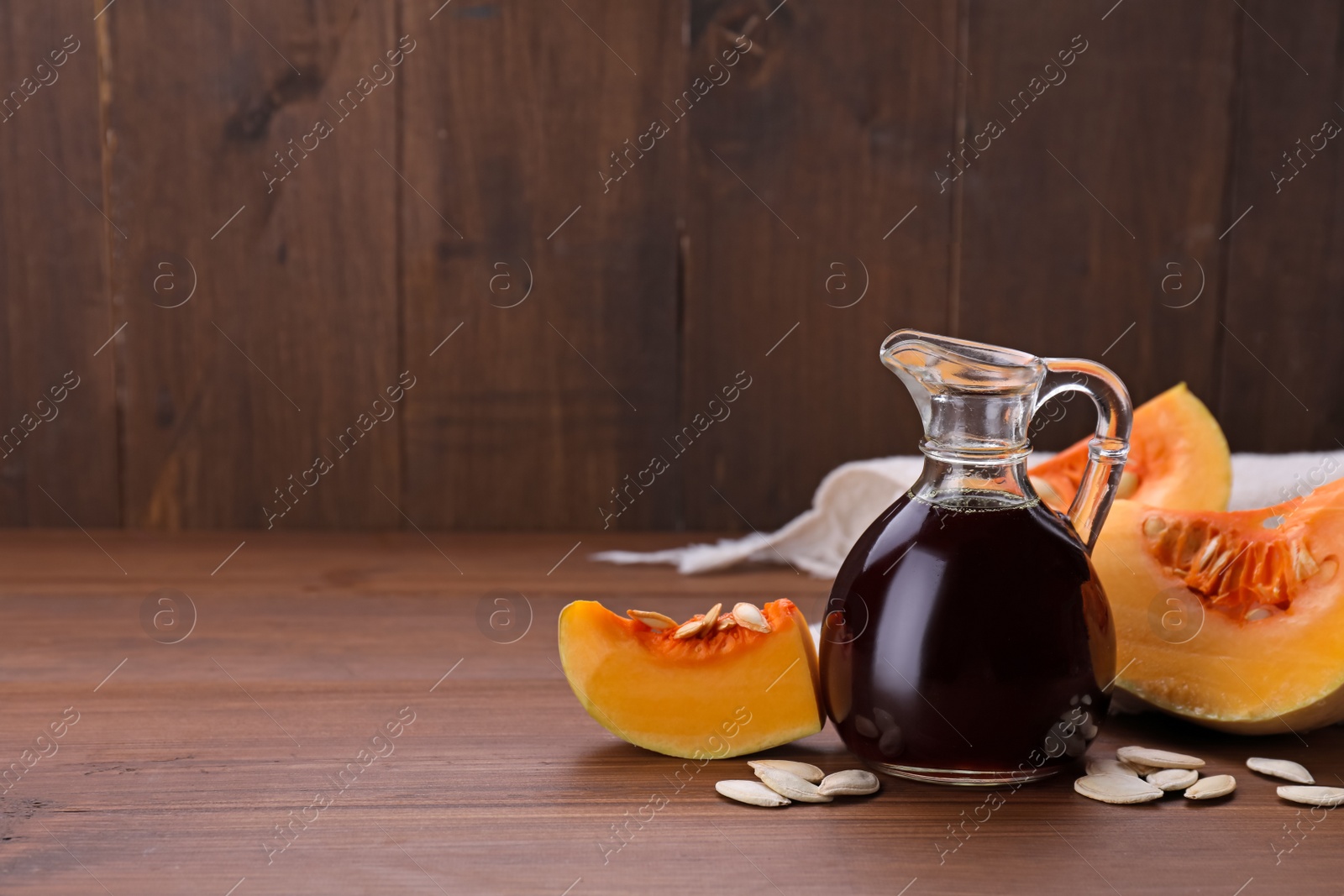 Photo of Fresh pumpkin seed oil in glass jug on wooden table. Space for text