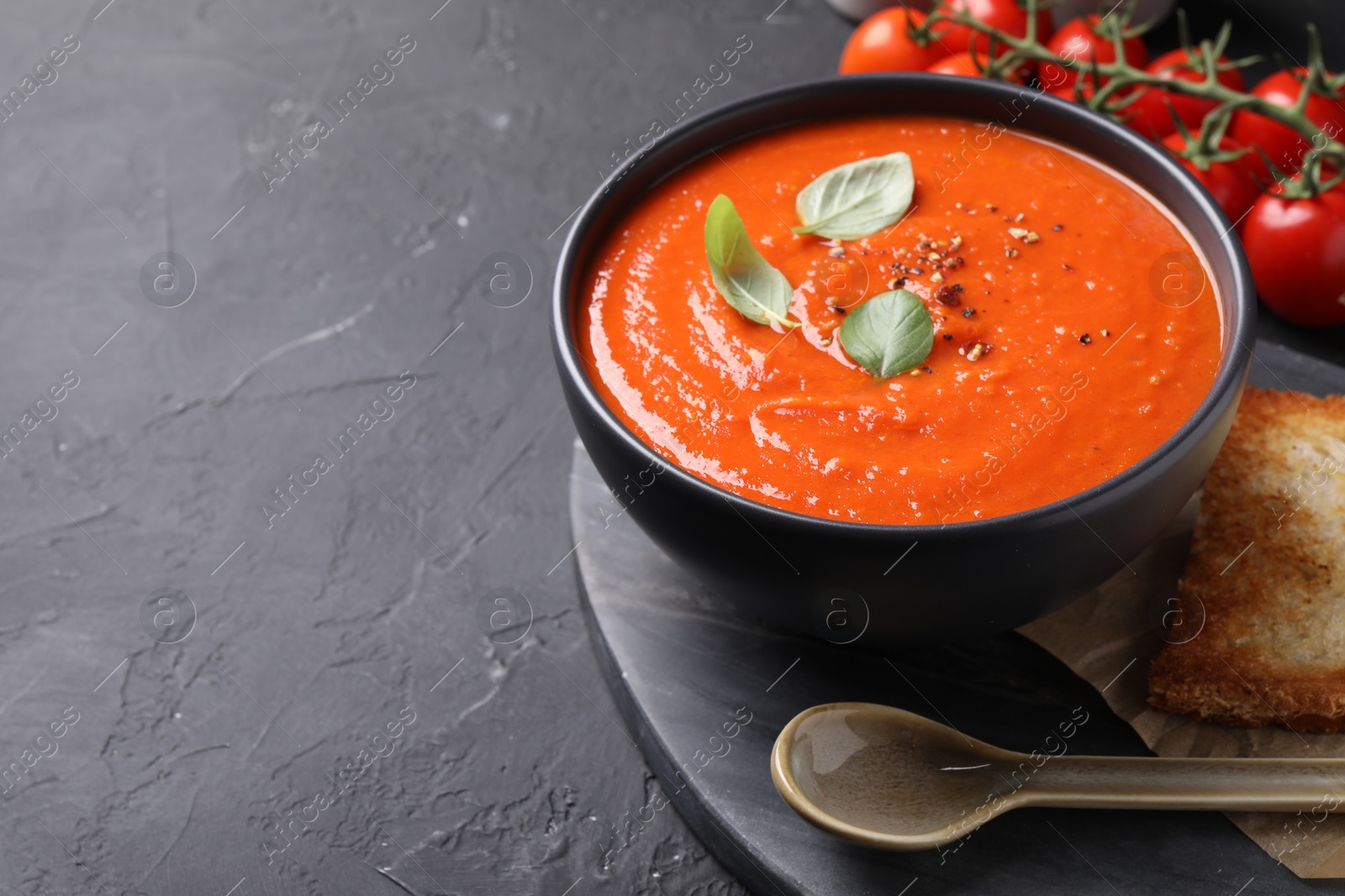 Photo of Delicious tomato cream soup served on black textured table. Space for text