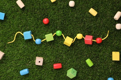 Photo of Wooden pieces and string for threading activity on artificial grass, flat lay. Educational toy for motor skills development
