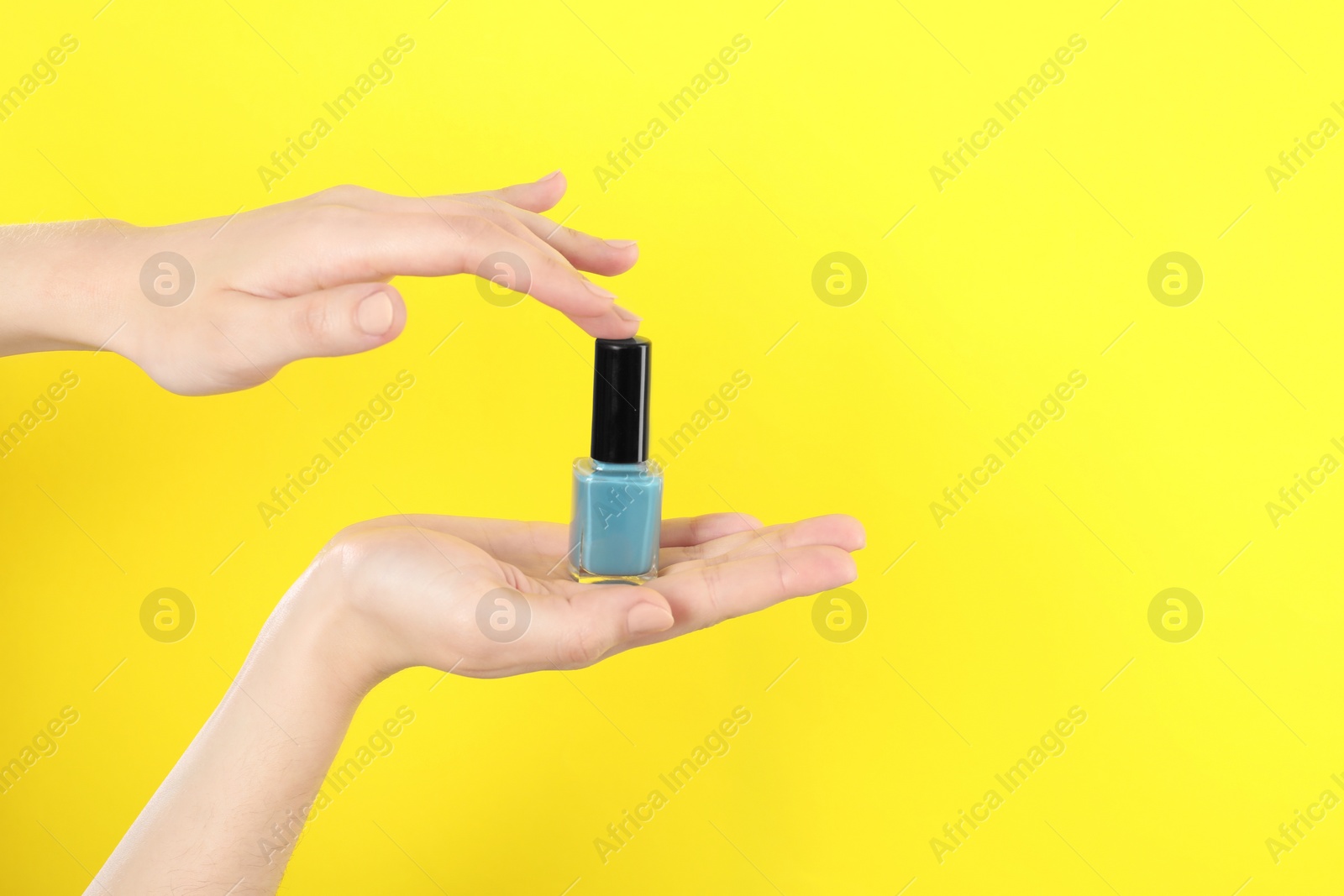 Photo of Woman holding nail polish on yellow background, closeup