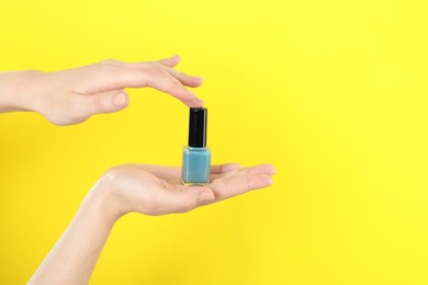 Photo of Woman holding nail polish on yellow background, closeup